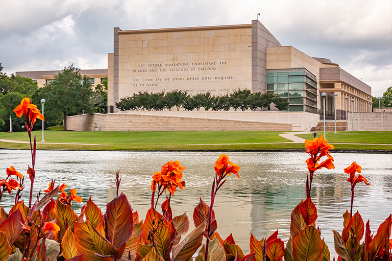 The George H.W. Bush Presidential Library reflected in the pond with orange canna lilies in the foreground